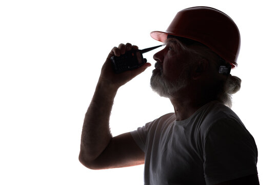 Silhouette of a senior construction worker in a hard hat talking on a walkie-talkie, isolated on a white background