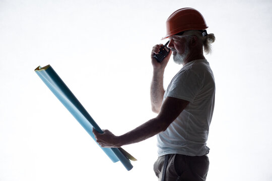 Silhouette of a senior construction worker in a hard hat talking on a walkie-talkie, isolated on a white background
