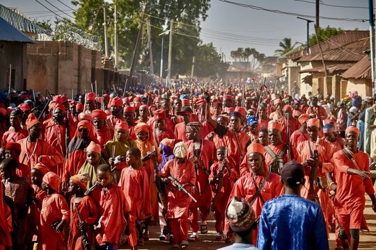 Zaria City, Nigeria - 21 March 2026: View of a vibrant crimson procession, a sea of red garments and traditional weapons, filling a dusty street with cultural fervor.