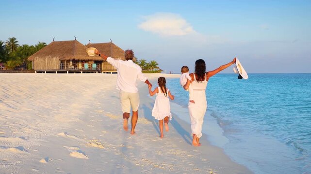Slow motion view of a happy family on holidays running on a tropical paradise beach in the Maldives islands during sunset time