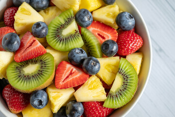 Obraz premium Fresh fruit salad bowl with sliced kiwi, strawberries, pineapple and blueberries. Healthy organic snack, colorful summer fruit mix, vegan breakfast food