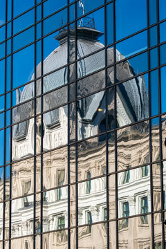Historic dome seen in reflection on modern glass building facade with grid windows creating strong contrast between classic architecture and new design