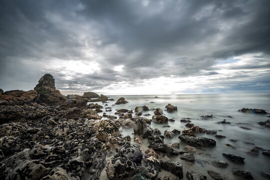 Rocky coast, rocks on the beach, dark rain clouds, long time exposure, West Coast, South Island, New Zealand