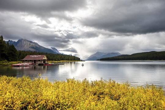 Curly Phillips Boathouse, historic boathouse on the shore of Maligne Lake, behind it mountain range Queen Elizabeth Ranges, autumn vegetation, cloudy sky, Jasper National Park, Rocky Mountains, Alberta, Canada