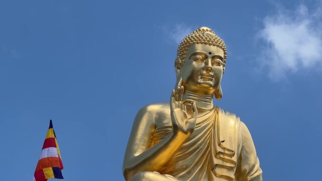 Golden Buddha statue shown from the waist up with raised blessing gesture against clear blue sky. Inner peace.