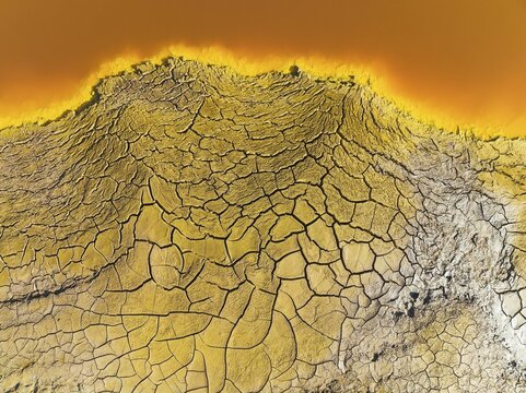 Cracked earth at the bank of the Rio Tinto (Red river) with its deep reddish hue due to oxidised iron minerals in its water, aerial view, drone shot, Huelva province, Andalusia, Spain
