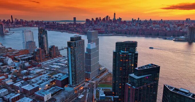 Stunning panorama of New York City crossed by the river. Spectacular orange sky at sunst in the backdrop. Aerial view.