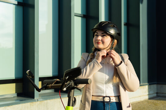 Young businesswoman buckling helmet on electric scooter