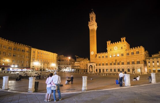 Tourists at the Palazzo Pubblico with illuminated Mangia Tower and chapel, night, Piazza Il Campo, Siena, Tuscany, Italy