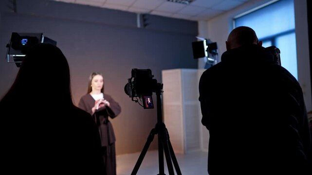 Rear view of the people working backstage during the footage. Man arranges equipment to record a video with a woman standing in the backdrop.
