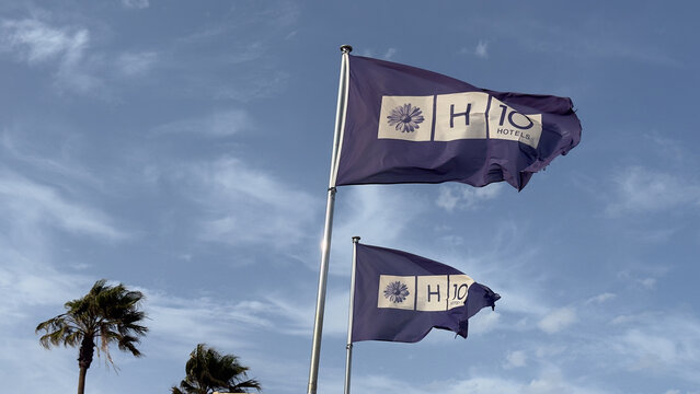 April, 5th 2026, Fuertaventura, Spain. H10 hotels flags waving strongly in wind against blue sky dynamic coastal weather and movement concept