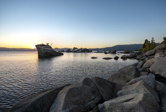 Lake shore, Bonsai Rock, small tree on a rock in the water at sunset, round stones in the water, Lake Tahoe, California, USA