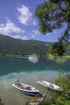 Small rowing boats and boat of the Wei&szlig;enseeschifffahrt arrives at the landing stage at Ronacherfelsen, Wei&szlig;ensee, Carinthia, Austria