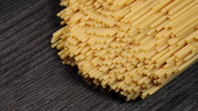 A pack of dry spaghetti pasta lies on a black wooden surface and slowly turns.