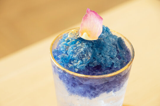 Blue shaved ice dessert with lotus petal top and gold rim glass, summer frozen treat topped with edible flower, refreshing icy texture and delicate