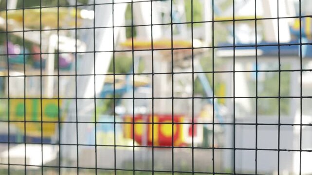 Black metal grid in foreground creates patterned overlay, partially obscuring vibrant amusement park rides in background.