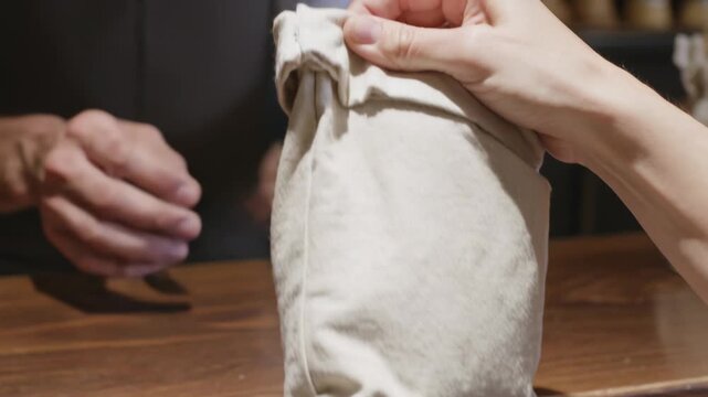 Rolled cuff exposing bread roll drawing customer reaching at bakery, aproned staff steadying bag