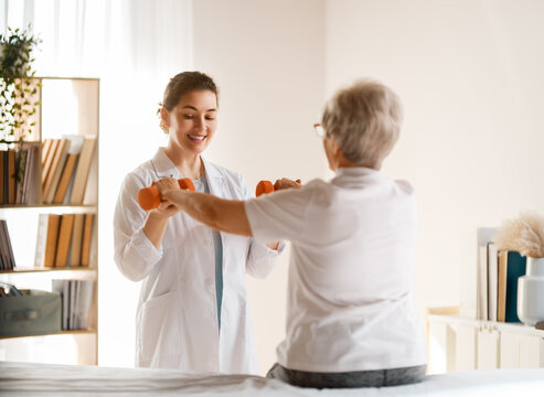 Smiling Female Physiotherapist Assisting Senior Woman with Dumbbell Rehabilitation Exercise at Home