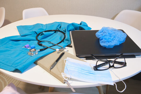 Healthcare worker scrubs, stethoscope, laptop, and protective wear on table, representing daily tasks