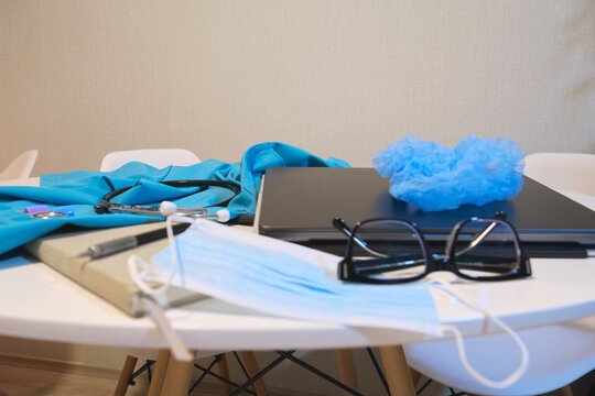 Medical uniform, stethoscope, laptop, and protective mask on a white desk, representing healthcare work