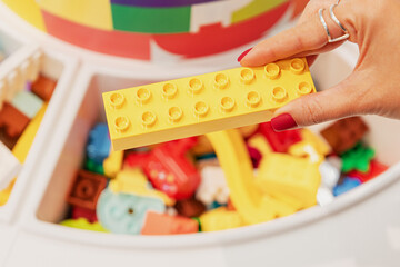 Naklejka premium 19 October 2025, Belgrade, Serbia: Hand holding a yellow plastic toy block, ready for creative building