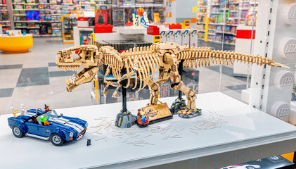 Naklejka premium 19 October 2025, Belgrade, Serbia: LEGO Tyrannosaurus Rex skeleton model displayed with a blue car in a bright modern toy store, showcasing popular brick built toys