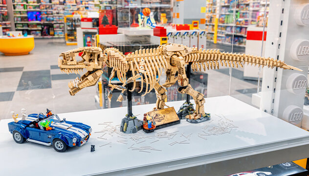 19 October 2025, Belgrade, Serbia: LEGO Tyrannosaurus Rex skeleton model displayed with a blue car in a bright modern toy store, showcasing popular brick built toys