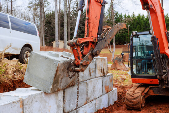 Excavator lifts concrete block from ground places it on retaining walls during construction site