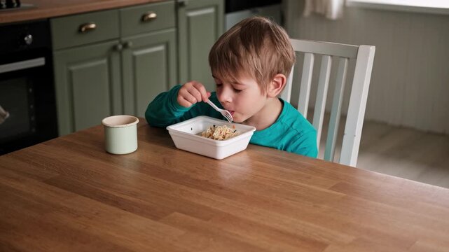 6 years old boy eats instant noodle from box. Child is eating Asian ramen. Lunch time. A good appetite. Tasty children food. Close-up portrait. Carbs dinner. Fast food. Kid eating by himself with fork