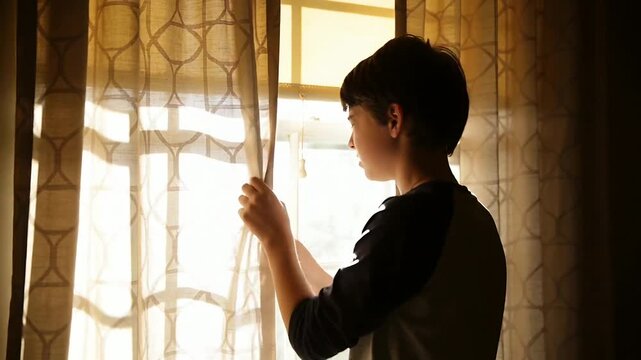 Squinting teen male pulling patterned sheer curtain at home, blocking bright sunlight, copy space