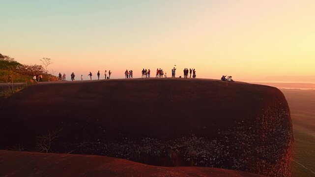 Epic sunrise at a famous Thai viewpoint, capturing tiny human figures on a colossal rock ledge above a sea of trees, evoking adventure, scale, and serenity.