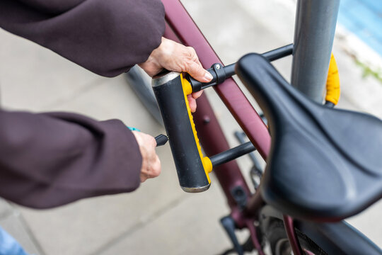 Senior Woman Securing Bicycle with U-Lock on City Street, close-up
 
