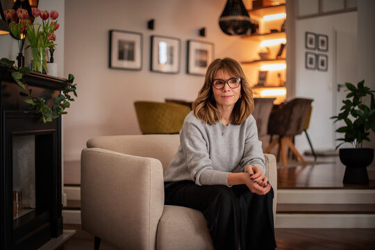 Blond haired attractive woman relaxing in an armchair in her modern apartment