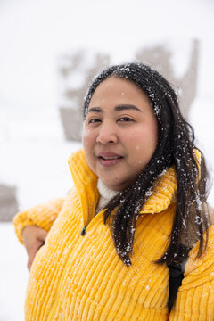 Portrait Young Asian fat woman smiles happily in falling snowflakes. smiling broadly. Wearing thick coat, Snowy landscape surrounds them, Joyful winter moment, family scenes. winter vacation