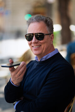 Confident mature man with smartphone sitting at table at sidewalk cafe