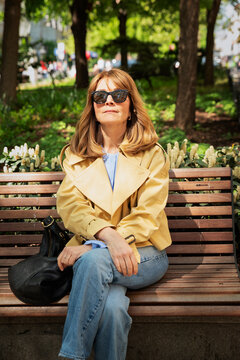 Confident blond haired woman sitting a park bench and enjoying the sunny weather