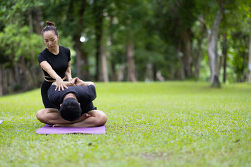 Naklejka premium People practicing outdoor yoga in a park guided by instructor, focusing on stretching and wellness while an instructor provides personal guidance to participant.