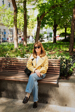 Confident blond haired woman sitting a park bench and enjoying a sunny day