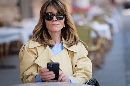 Confident blond haired woman with smartphone sitting in an outdoor cafe in the city