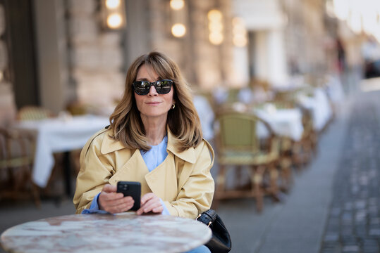 Confident blond haired woman with smartphone sitting in an outdoor cafe in the city