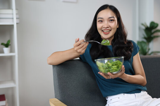 Beautiful healthy Asian woman happily eating delicious vegetable salad at home. Beautiful girl in enjoy eat clean vegetables after exercise for health in house. Diet and Healthy food.