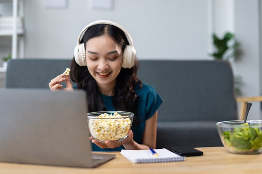 Young woman watching a movie on laptop and eating popcorn at home.