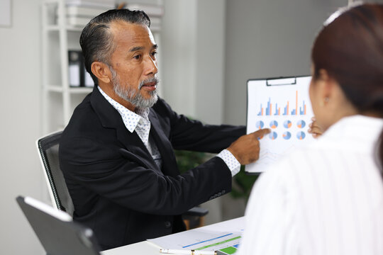 Business colleagues collaborating mentor pointing discussing ideas. Two business people, a senior man and a young woman, discussing business strategy while pointing at data reports.
