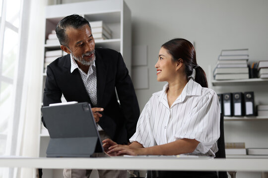 Senior man mentoring young Asian woman working in office.