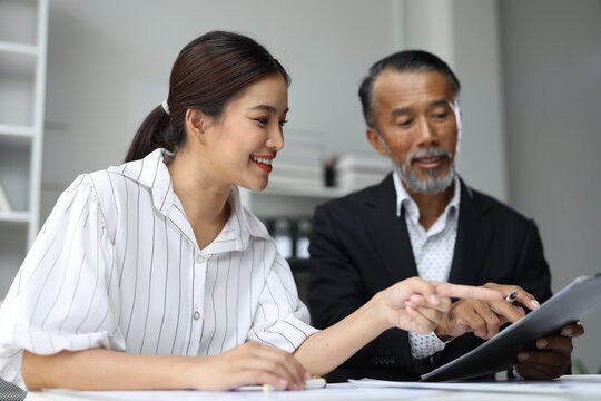 Asian executive mentors a young female colleague in office, reviewing documents and strategy together, teamwork, guidance and professional development.
