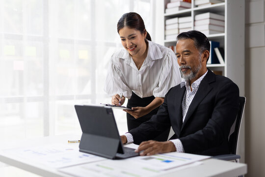 Asian business professionals discussing documents and reviewing data on a digital tablet in office.