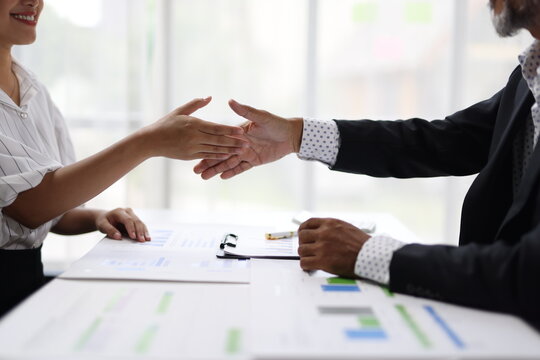 Business partners shaking hands finalizing agreement in office, shaking hands across a white desk, symbolizing an agreement, partnership, deal, or successful job interview in office.