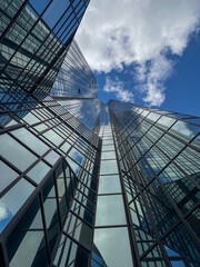 Obraz premium Glass skyscraper reflecting white clouds in blue sky.