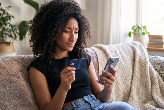 Woman holding credit card and phone, looking confused with online shopping or banking problem
