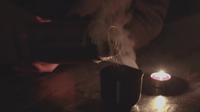 Pouring hot drink from thermos by candlelight during power outage